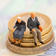 Zwei Figuren, eine Rentnerin und ein Rentner, sitzen auf einem Geldstapel.